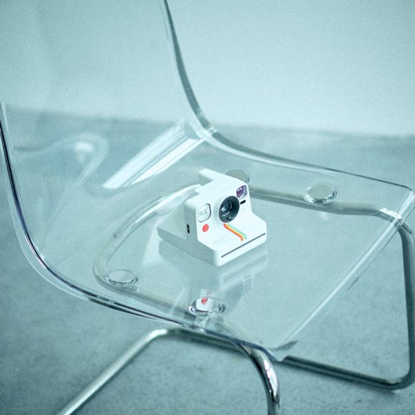 cry-25ss-lookbook-instant-camera-chair An instant camera placed on a transparent plastic chair, featured in the CRY SS25 Lookbook to evoke playful and candid lifestyle moments